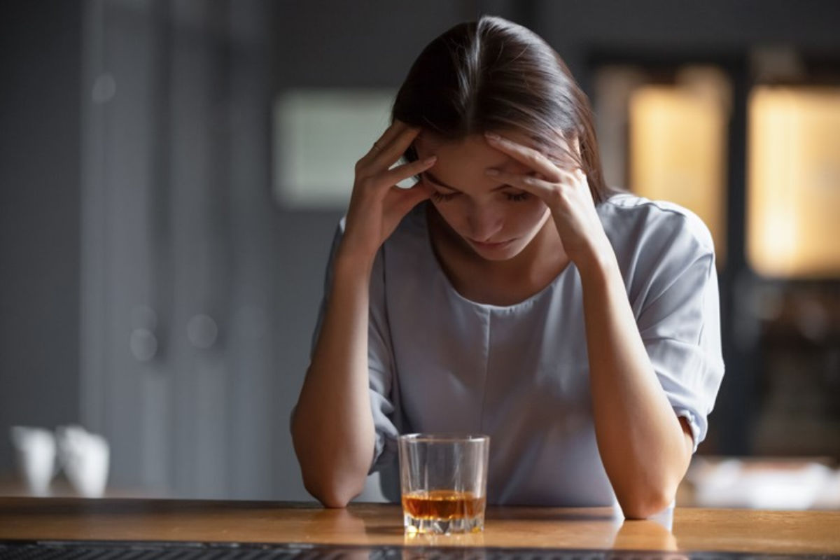 Una mujer pensativa delante de una bebida alcohólica