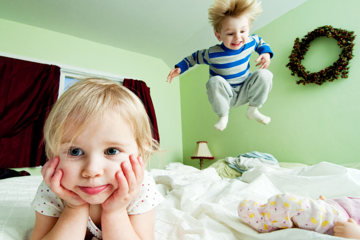 Niño hiperactivo salta en la cama junto a su hermana